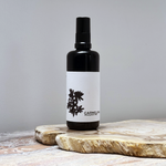 Load image into Gallery viewer, Black spray bottle with a white label on a wooden surface against a gray background
