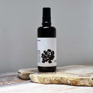 Black spray bottle with a white label featuring a black rose design on a wooden surface.
