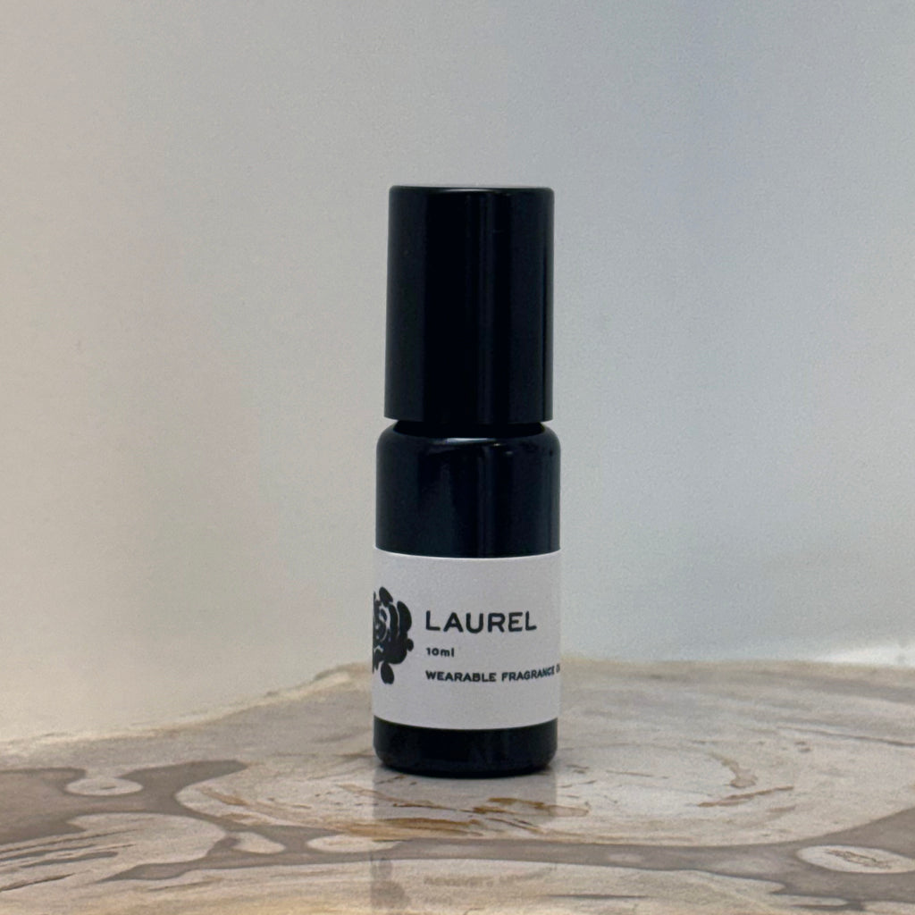 Black and white bottle of Laurel wearable fragrance oil on a wooden surface with a gray background