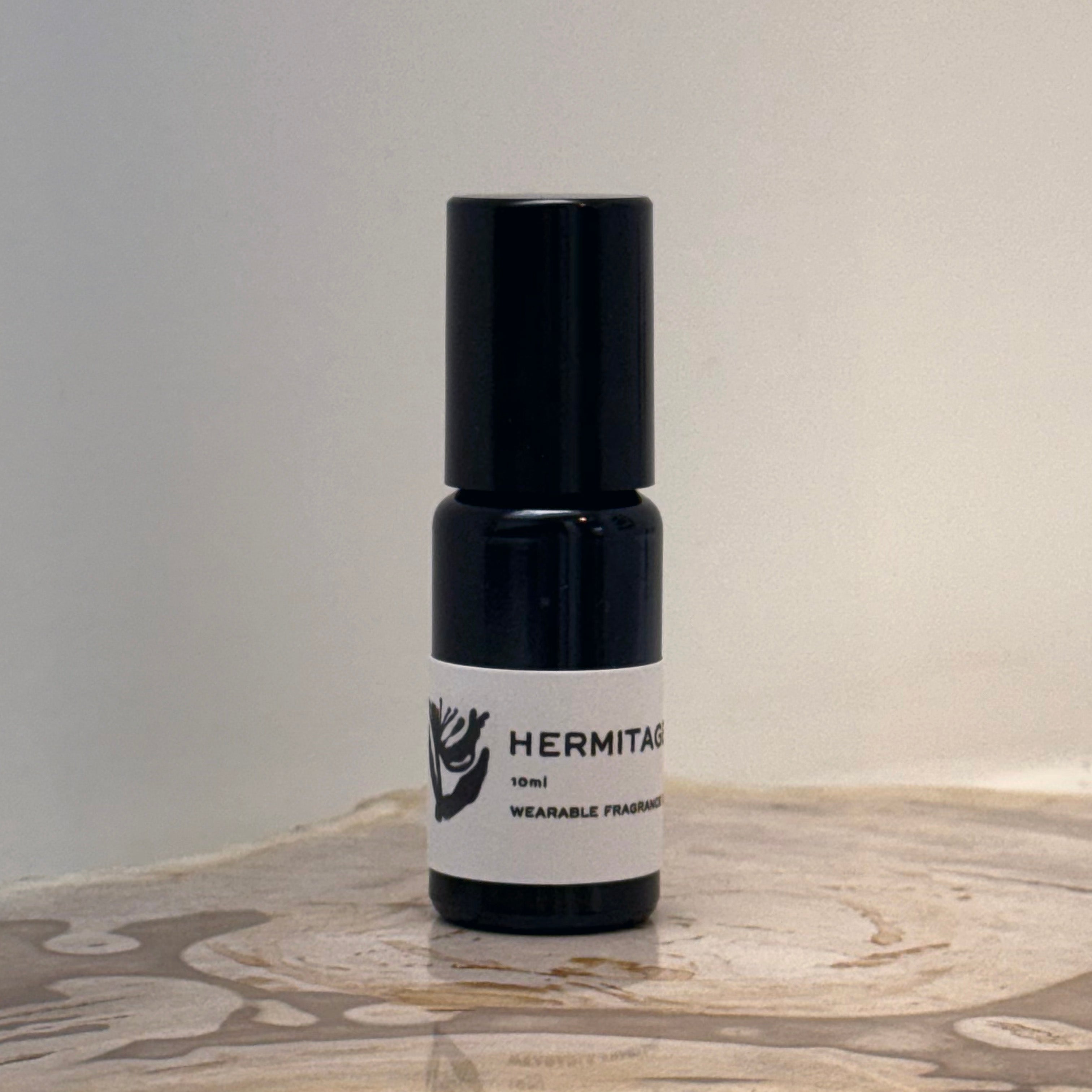 Black and white bottle of Hermitage perfume on a wooden surface with a neutral background