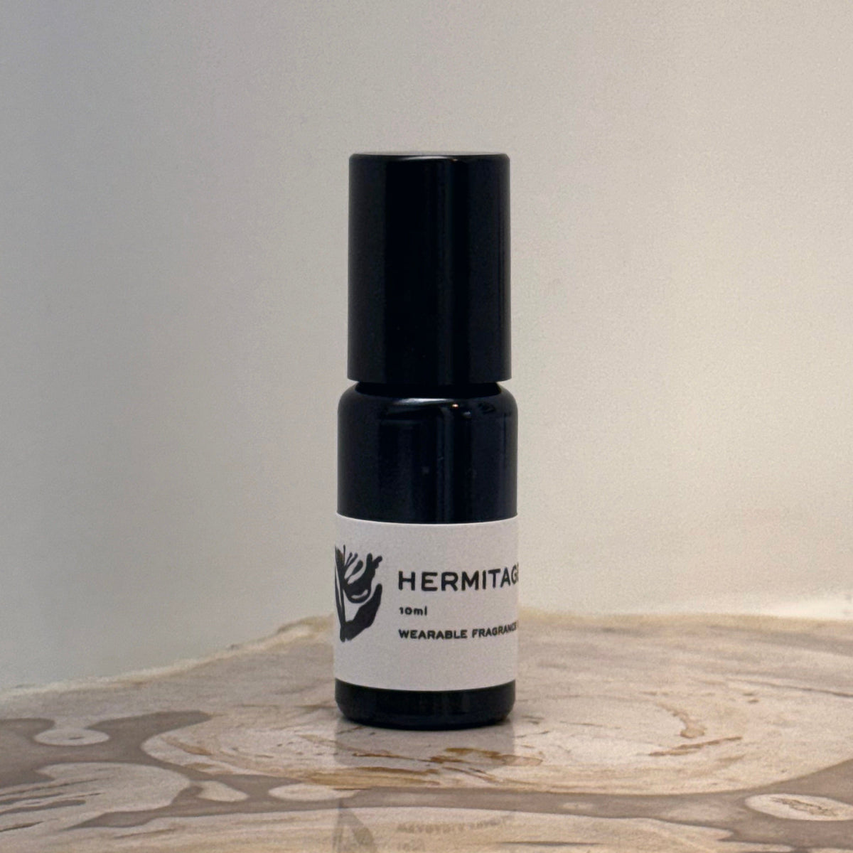 Black and white bottle of Hermitage perfume on a wooden surface with a neutral background