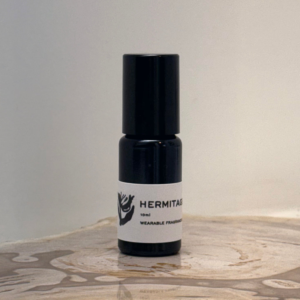 Black and white bottle of Hermitage perfume on a wooden surface with a neutral background
